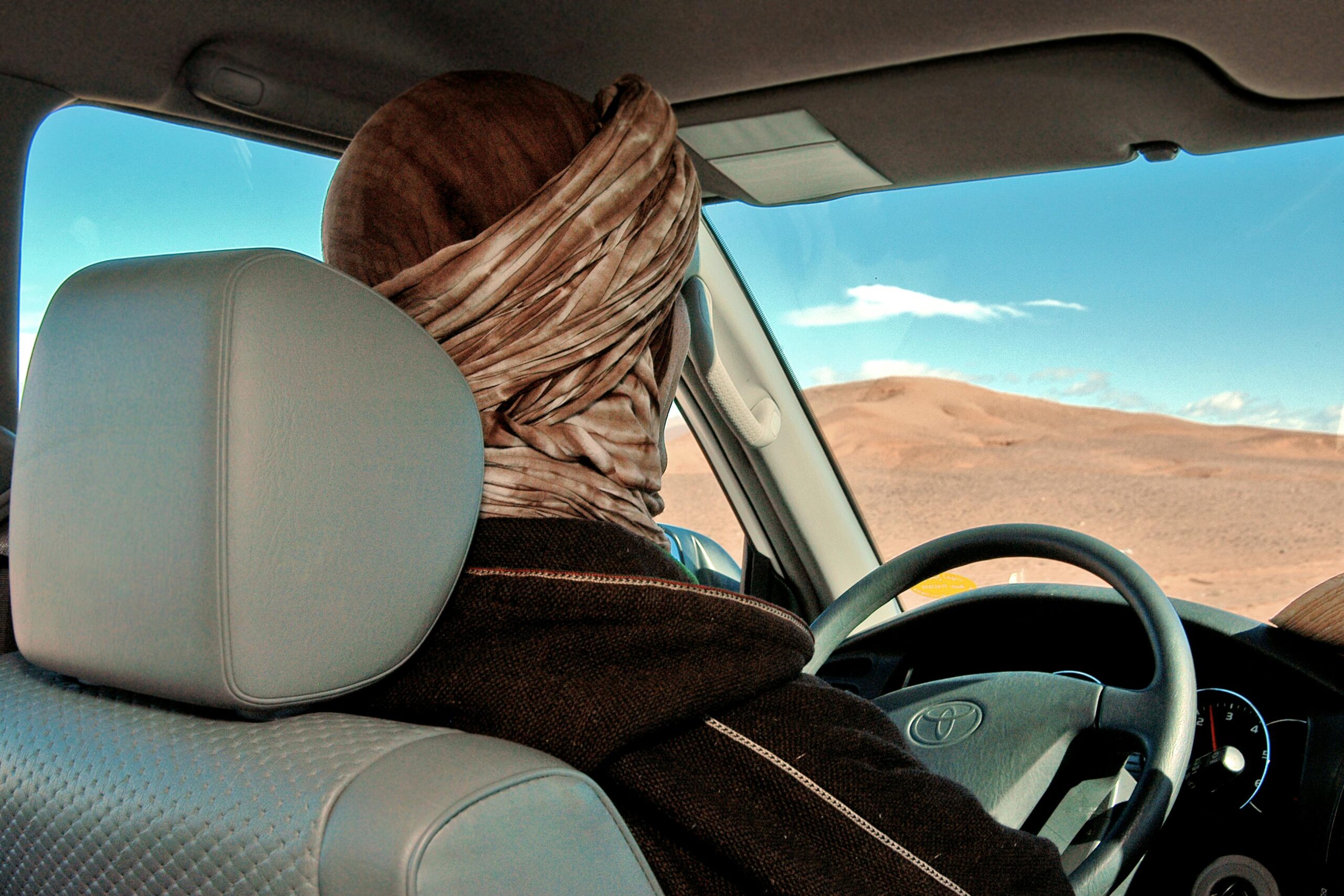 A person with a turban drives through the scenic Agafay desert in a vehicle.