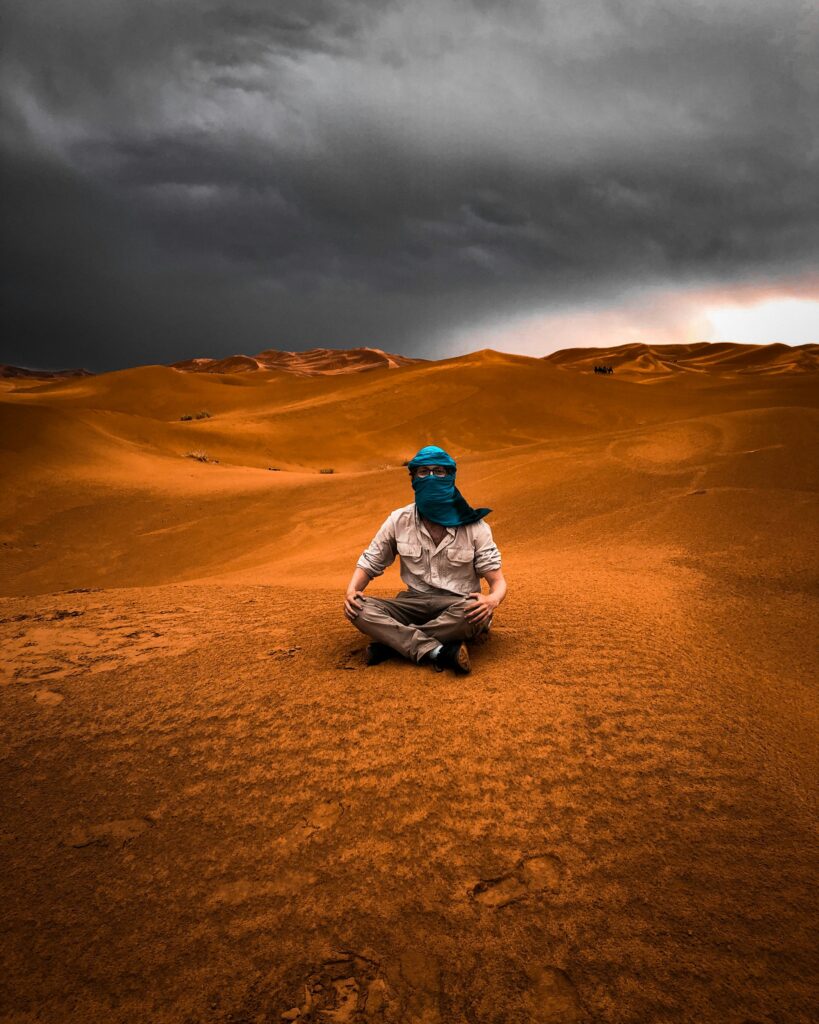 About us Traveler sitting in the Morocco Sahara Desert under dramatic skies